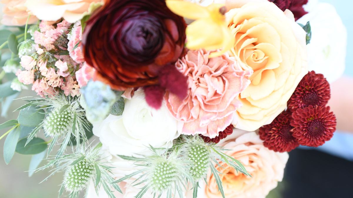 Bouquet of burgundy ranunculus, peach roses and thistle