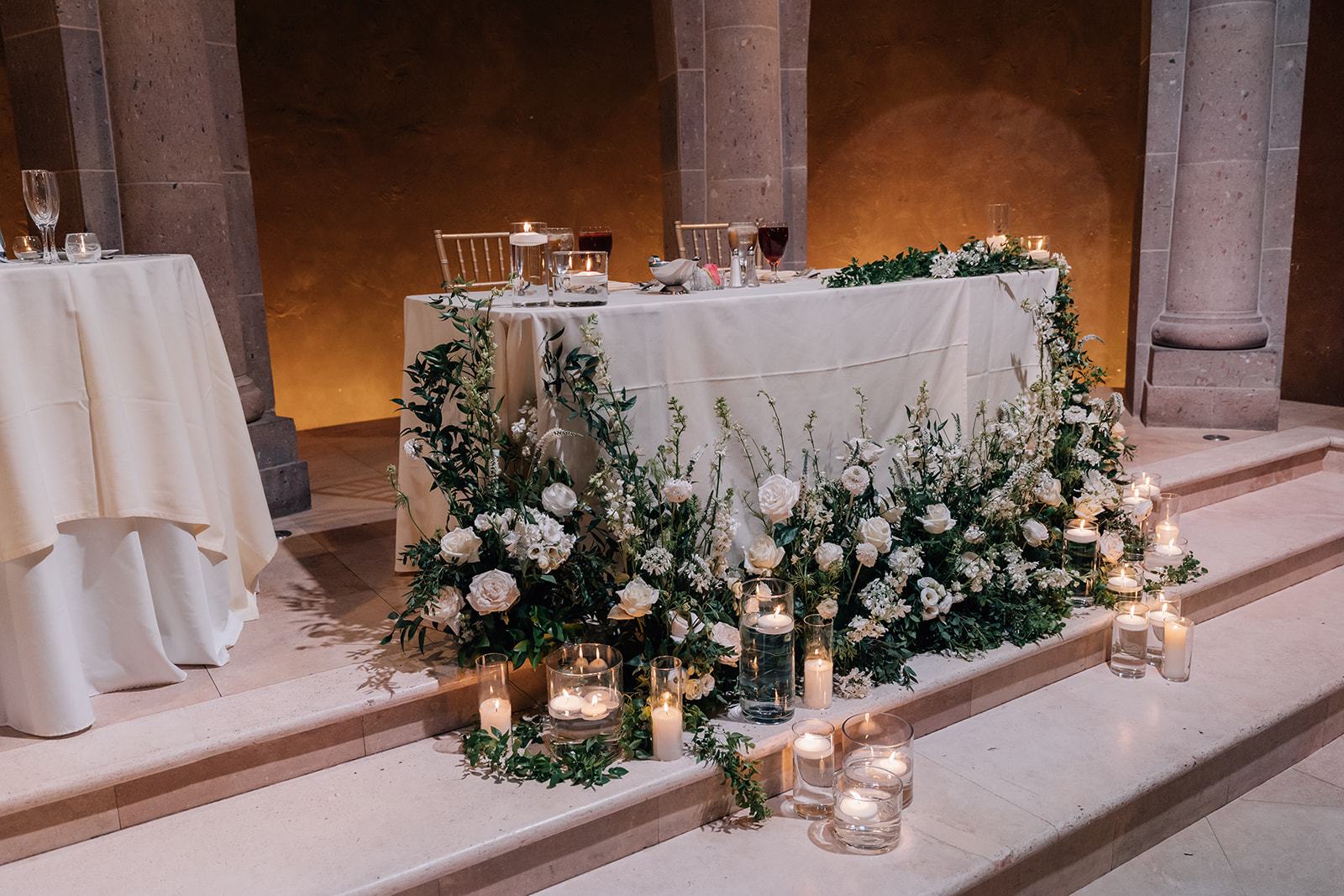 Head table edged with white blooms and candlelight
